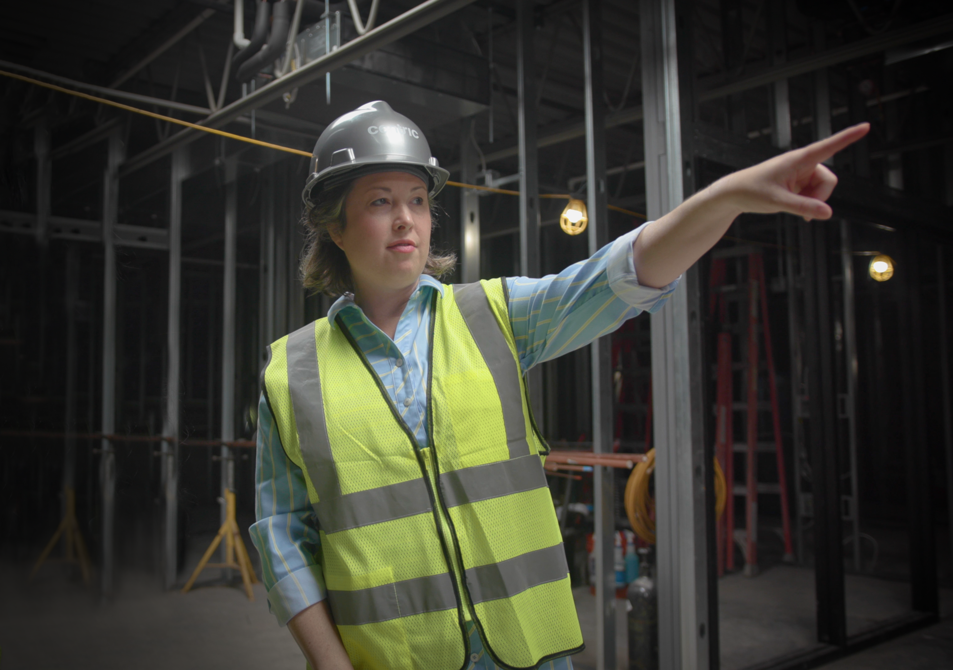 Woman mearing a construction vest on a construction site looking and pointing to her left